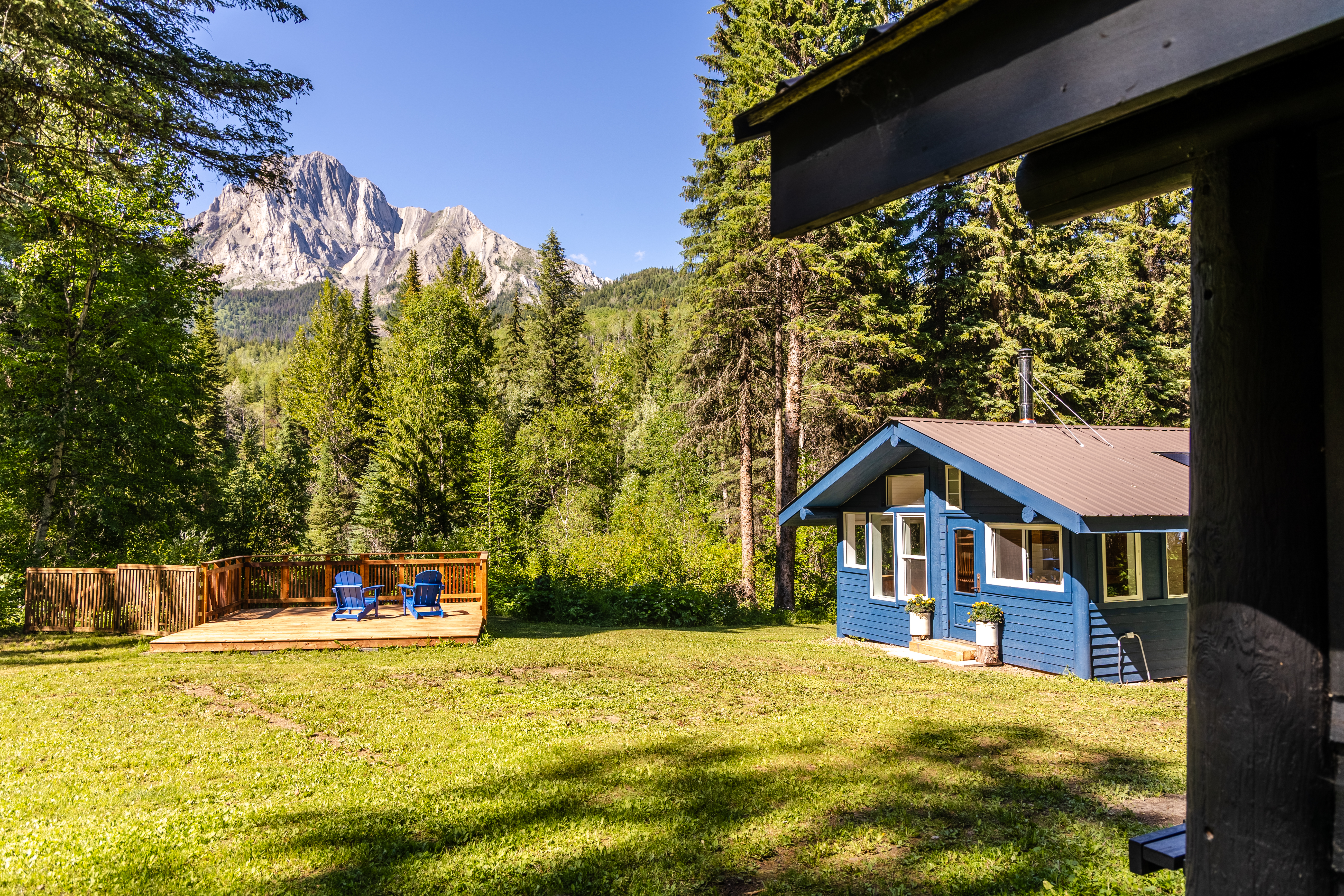 A blue cabin in a grassy field with a deck and mountains in the background.